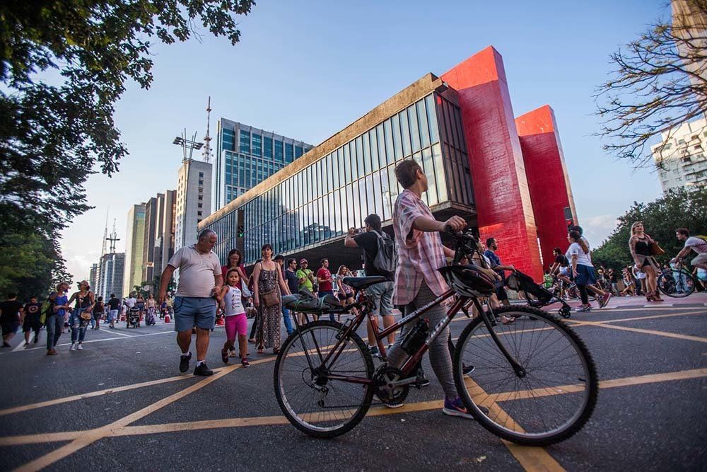 A man is riding a bike down a street in front of a large red building.