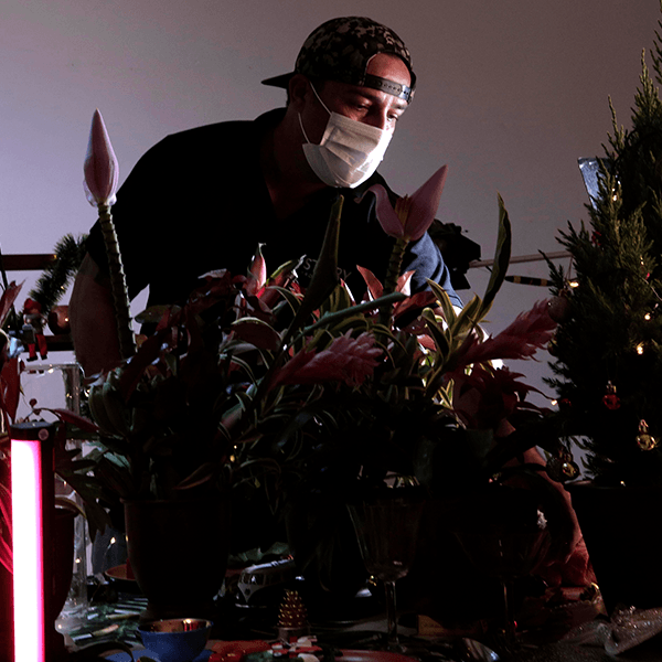 A man wearing a mask is arranging flowers in front of a christmas tree