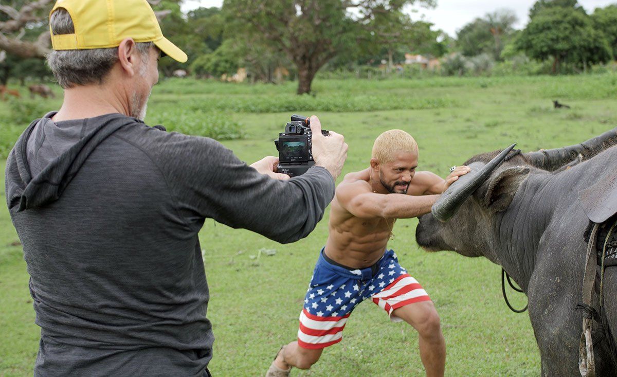 A man is taking a picture of a man fighting a water buffalo in a field.