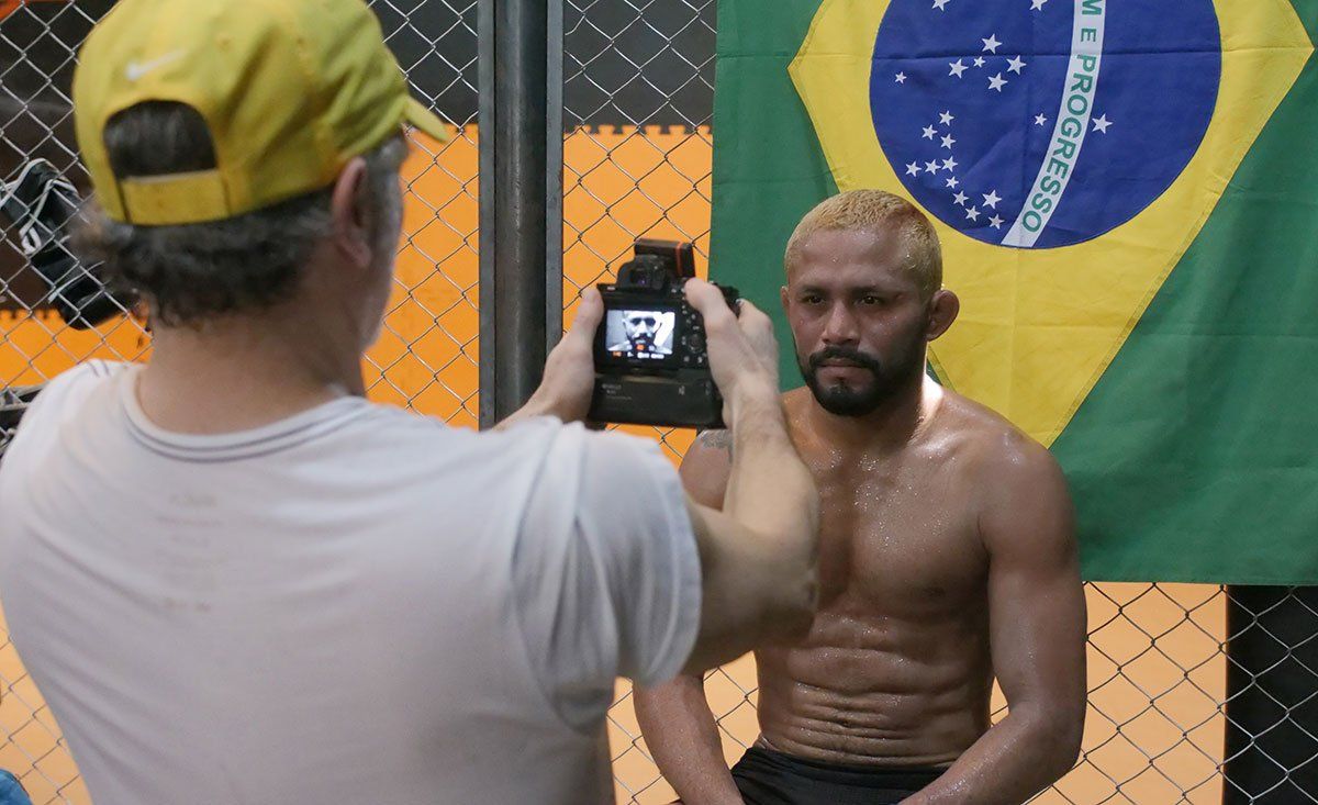 A man is taking a picture of a shirtless man in front of a brazilian flag.