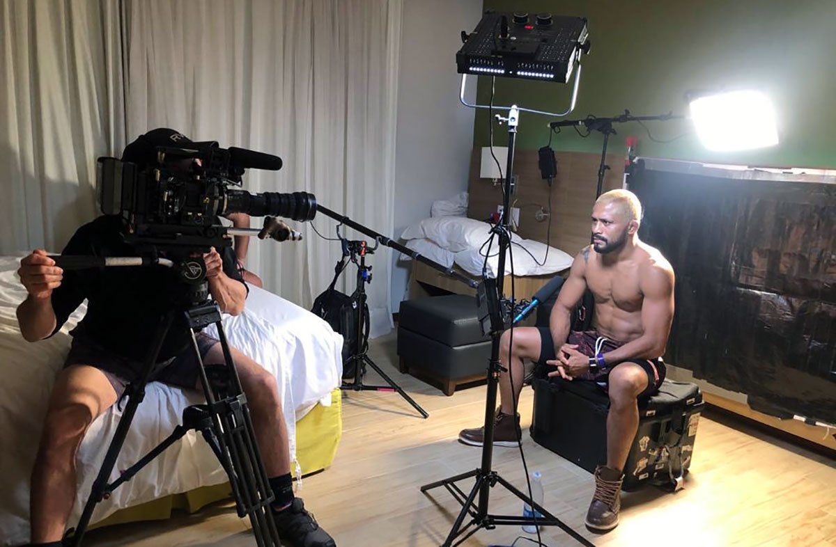 A man is sitting on a chair in front of a camera in a room.