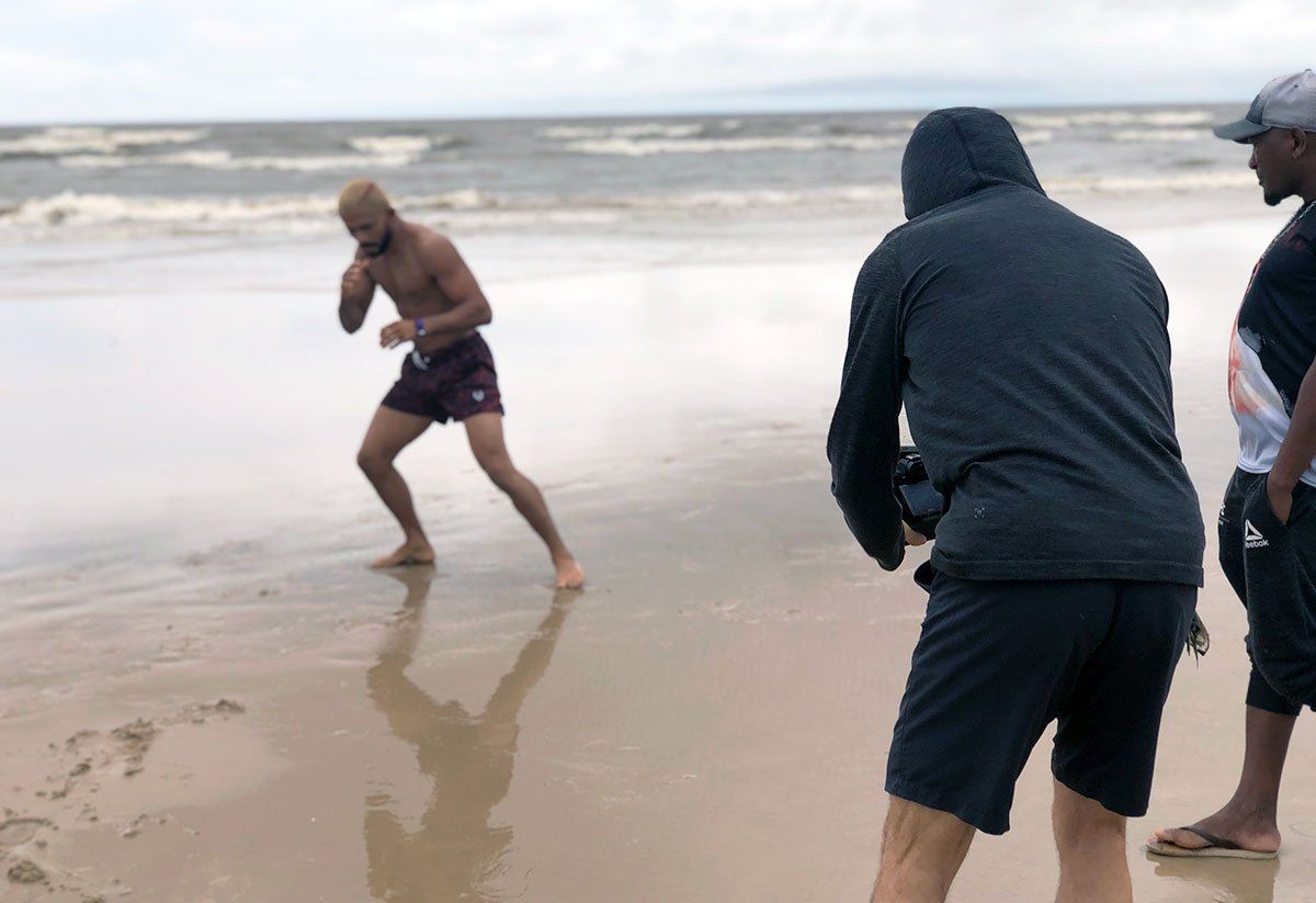 A man is standing on a beach taking a picture of another man.