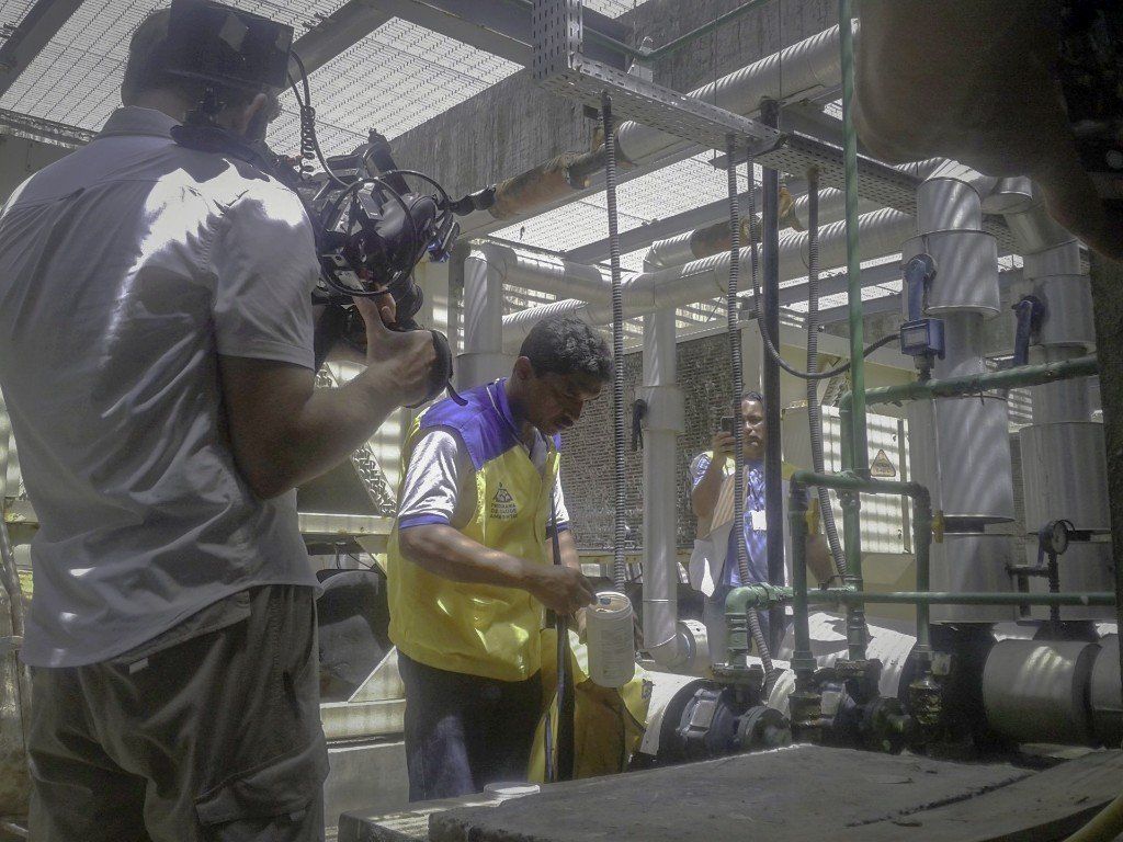 A man is taking a picture of a man in a yellow vest in a factory.