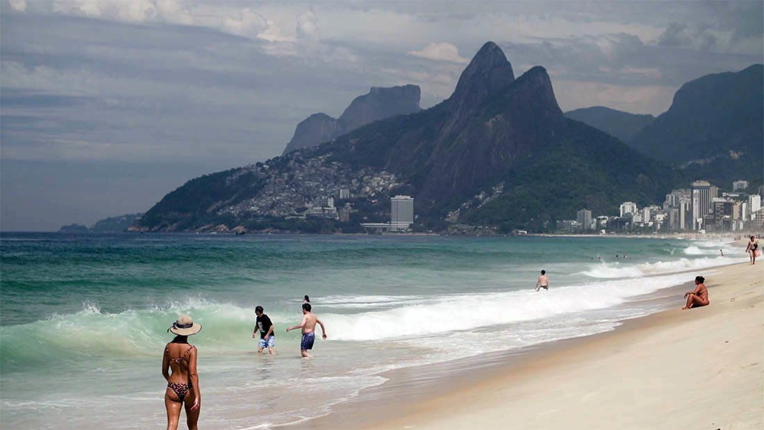 A group of people are standing on a beach with mountains in the background.