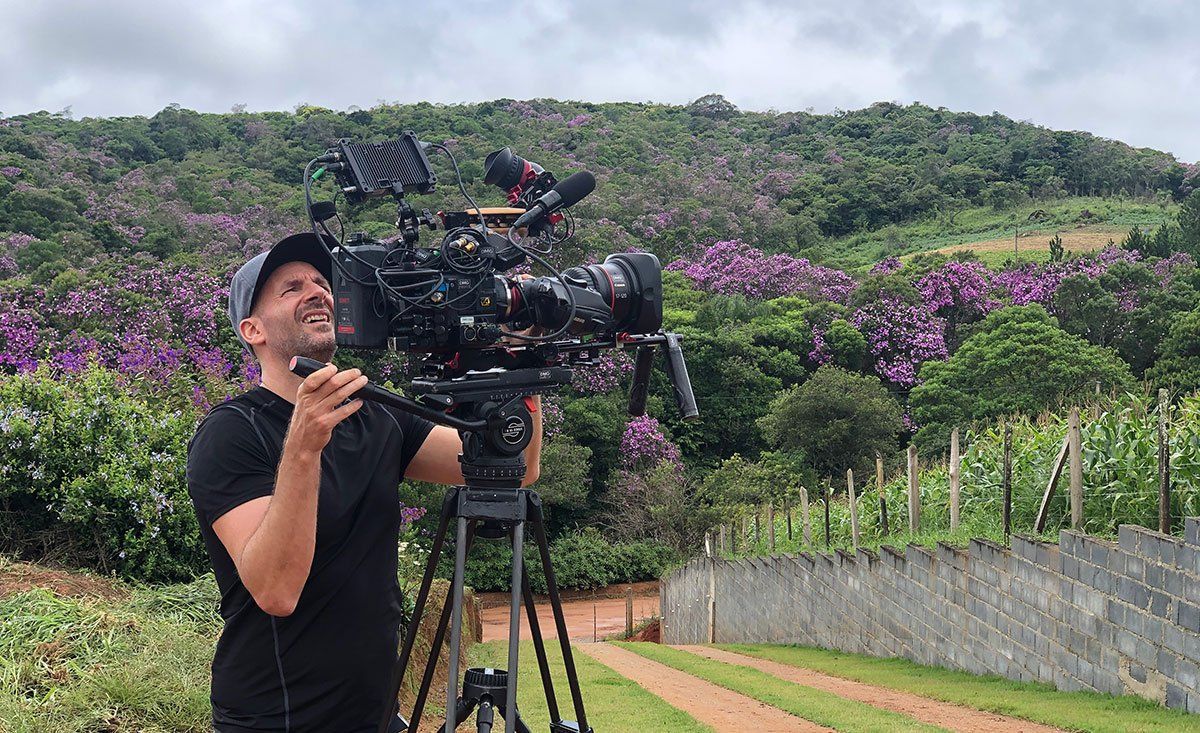 A man is holding a camera on a tripod in a field.