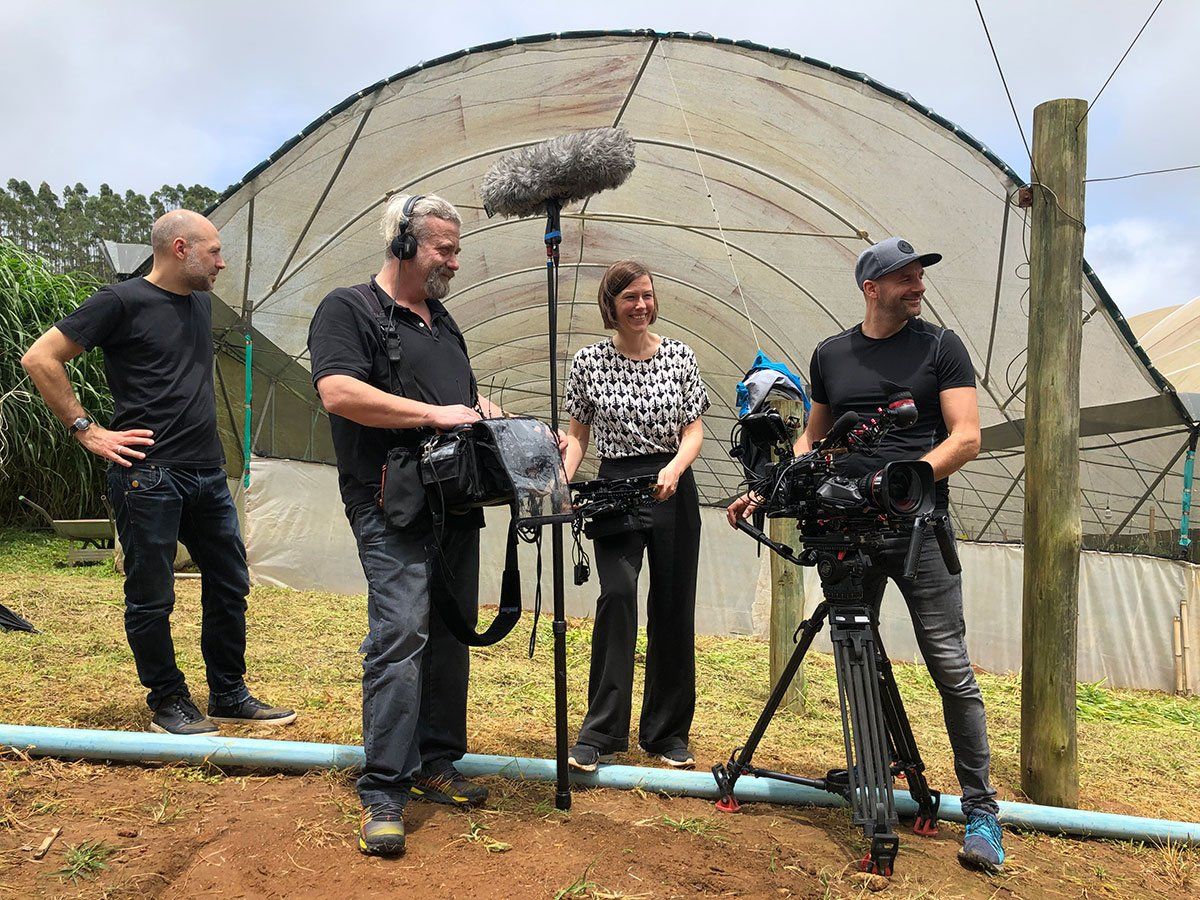 A group of people are standing in front of a greenhouse.