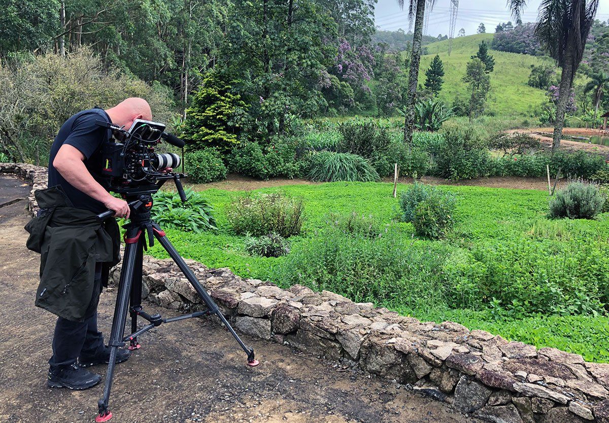 A man is standing in front of a camera on a tripod in a field.