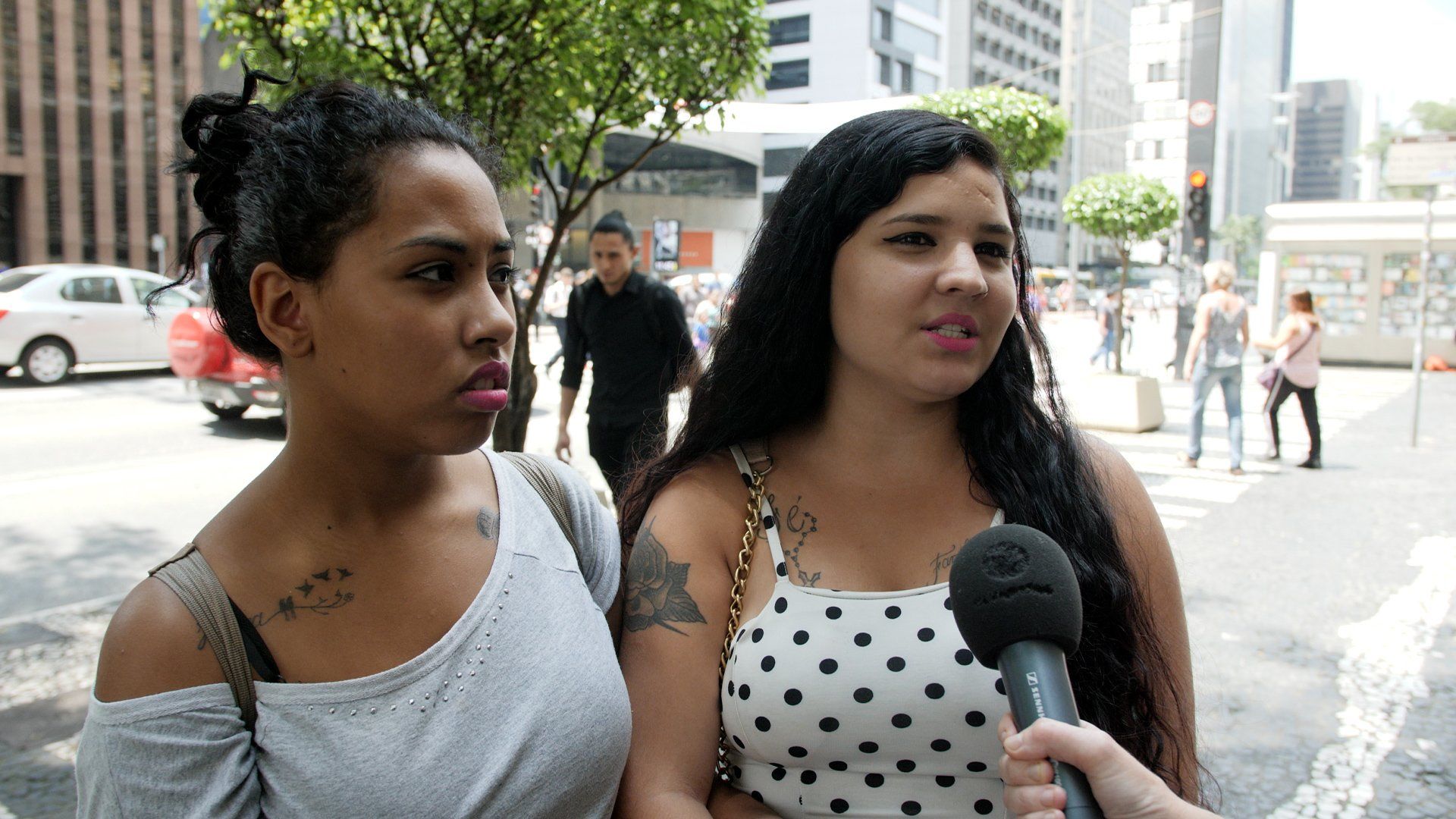 Two women are talking into microphones on a city street.