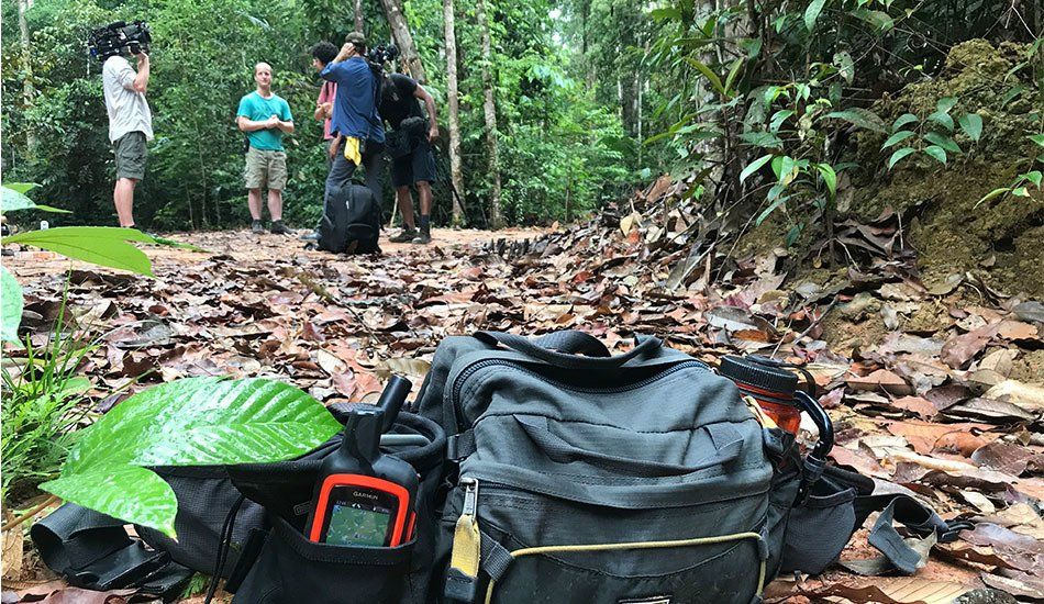 A group of people are standing in the woods behind a bag and a walkie talkie.