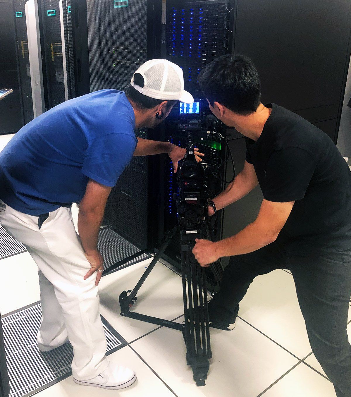 Two men are working on a camera in a server room