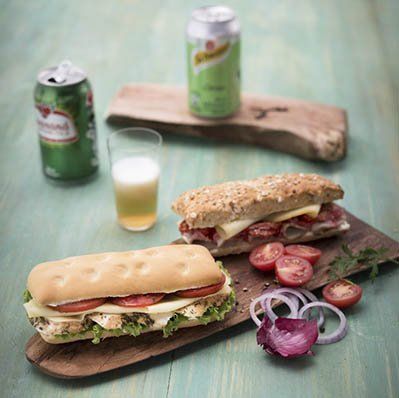 Three sandwiches are sitting on a wooden cutting board on a table.