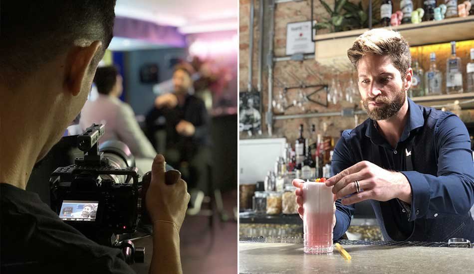 A man is taking a picture of a bartender preparing a drink.