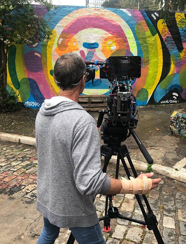 A man is holding a camera on a tripod in front of a colorful wall.