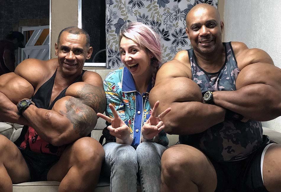 A woman is sitting on a couch next to two men with huge muscles.