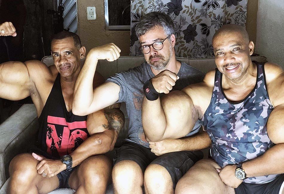 Three men are sitting next to each other and flexing their muscles.