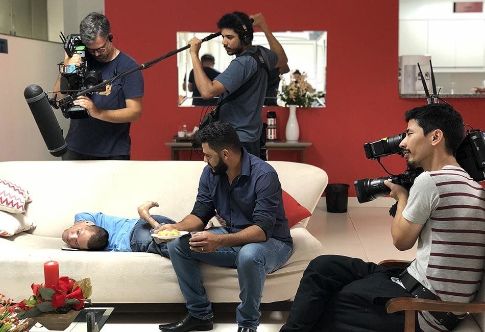A man is laying on a couch while a group of men film him