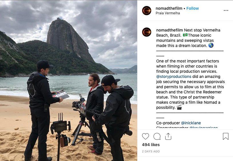 A group of men are standing on a beach with a mountain in the background.