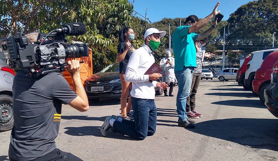 A man is kneeling down in front of a camera in a parking lot.