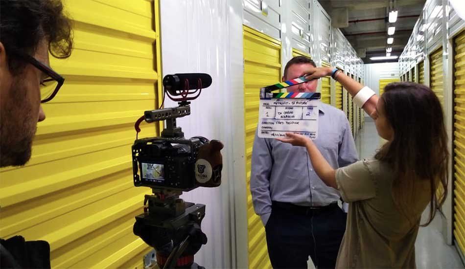 A woman is holding a clapper board in front of a man in a hallway.
