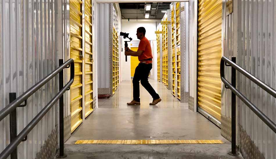 A man is walking down a hallway holding a camera.