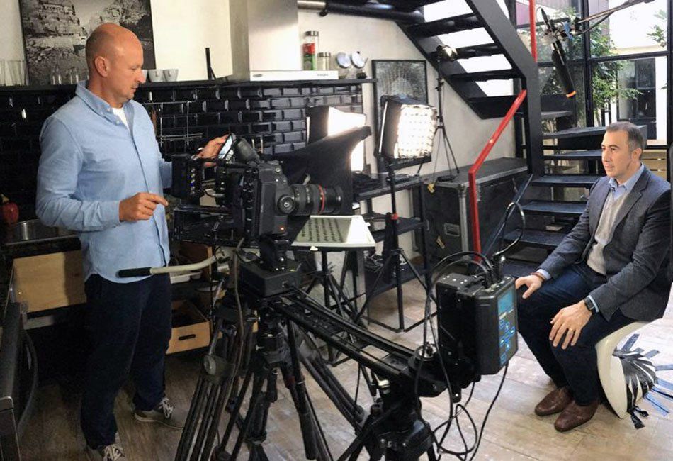 Two men are sitting in front of a camera in a room.