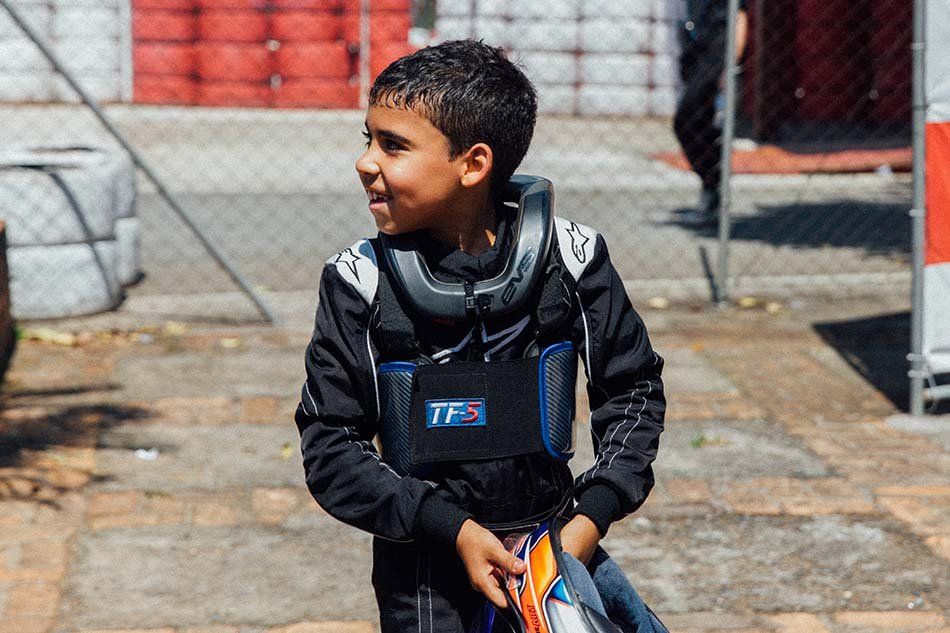 A young boy is wearing a racing suit and holding a helmet.
