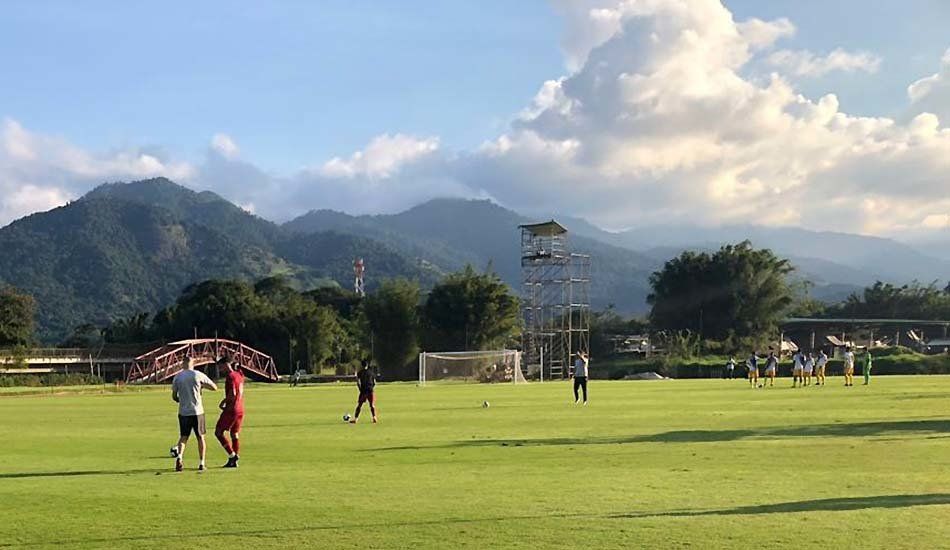 A group of people are playing soccer on a field with mountains in the background.