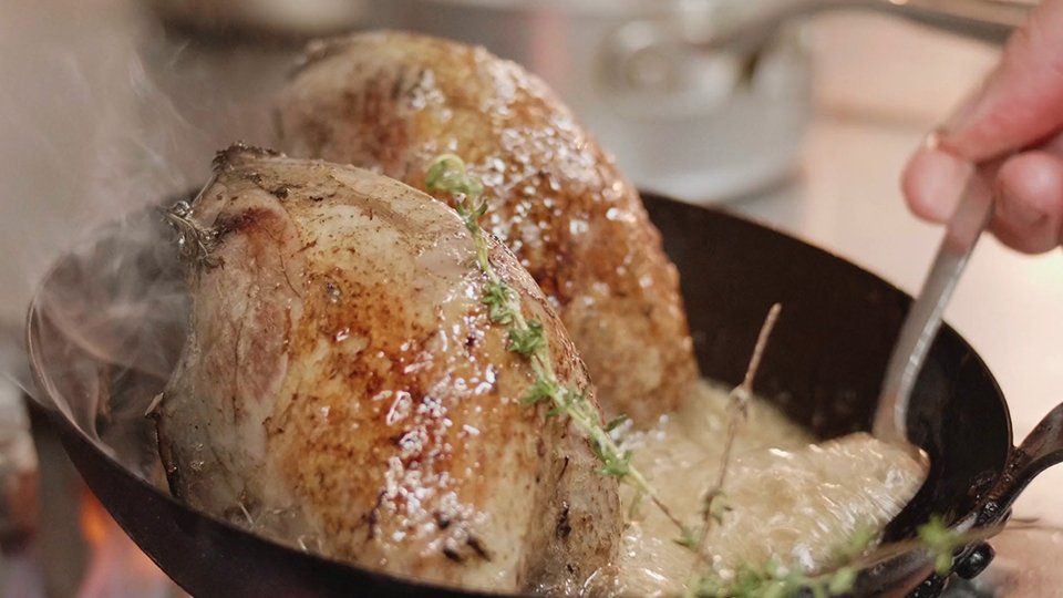 A person is cooking meat in a frying pan on a stove.