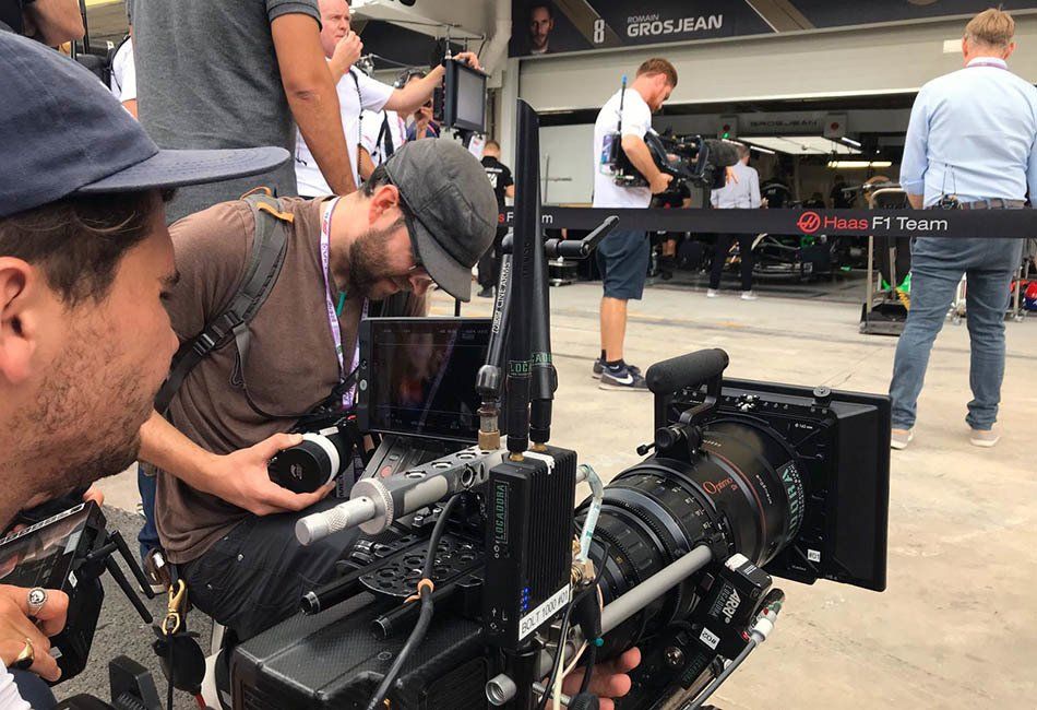 A man is looking at a camera while another man looks on.