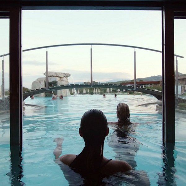 Two women are swimming in a pool with a bridge in the background