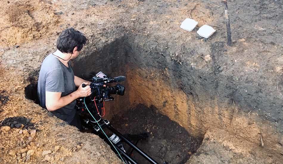 A man is sitting in a hole holding a camera.