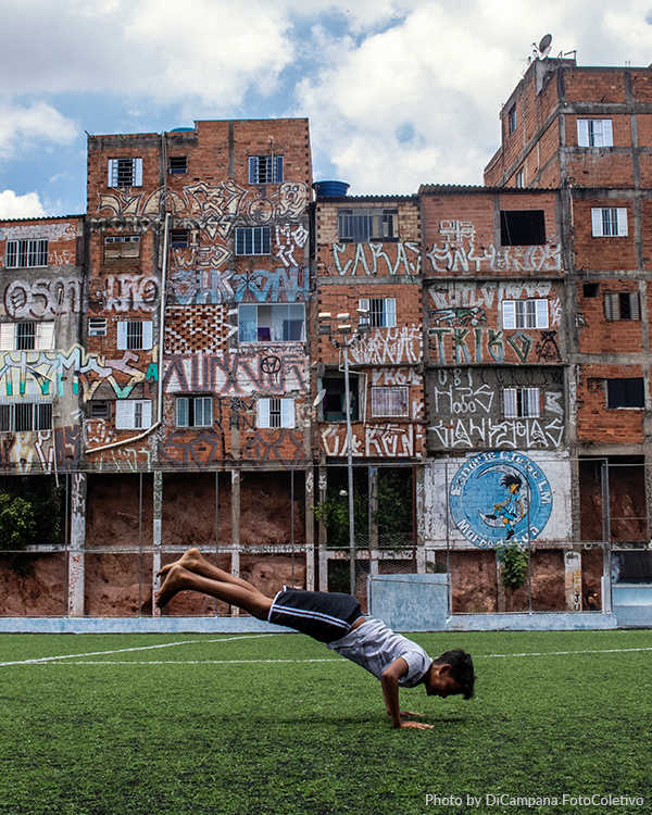 Photo by DiCampana Colectivo A young boy is doing a handstand on a soccer field in front of a building with graffiti on it.