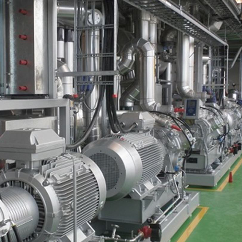 Industriële machines in een fabriek, met grote zilverkleurige turbines, leidingen en elektrische apparatuur op een rij.