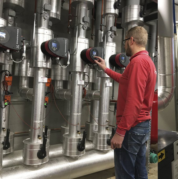 Technicus in rood shirt stelt bedieningselementen af op industriële leidingen en pompen in een machinekamer.