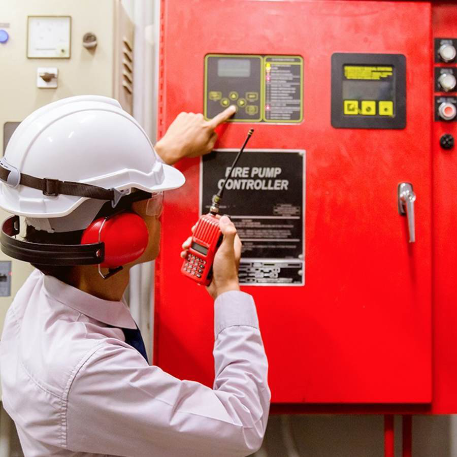 Een werknemer met een veiligheidshelm test een rode brandweerpompcontroller met een radio en een handmeter.