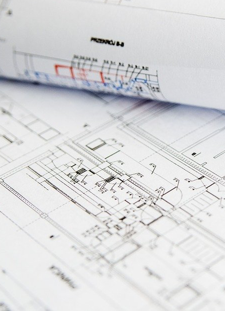 Architectuurtekeningen liggen uitgespreid op een bureau, met een opgerolde plattegrond waarop markeringen in rood en blauw te zien zijn.