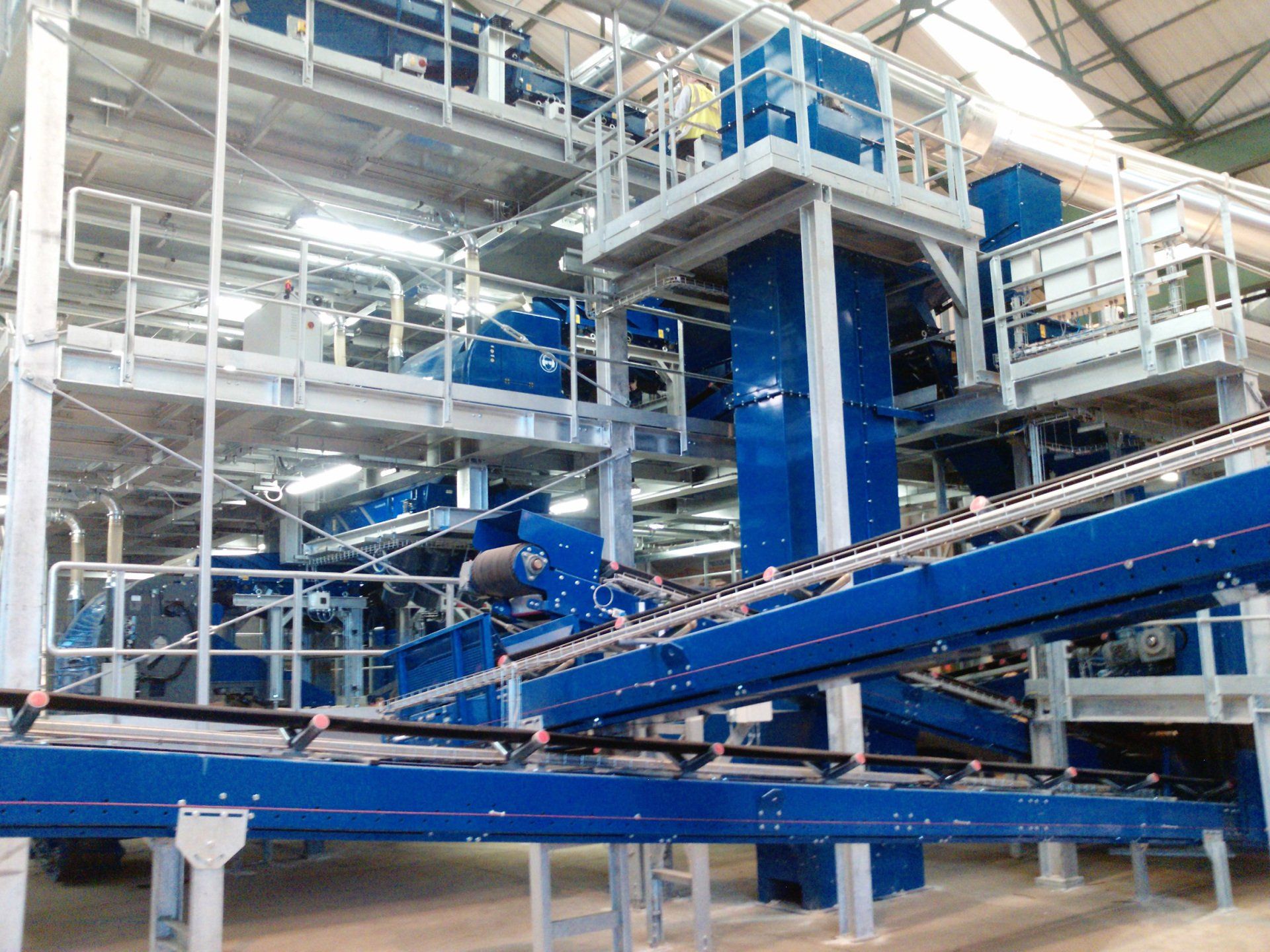 Industrieel transportsysteem met blauwe machines en metalen loopbruggen in een fabriek.