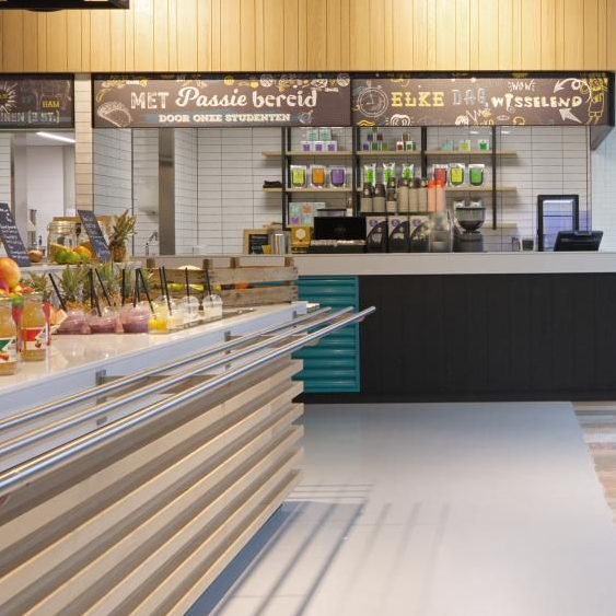 Moderne cafébalie met gebak, drankjes en een zwarte kassa onder een houten menubord.