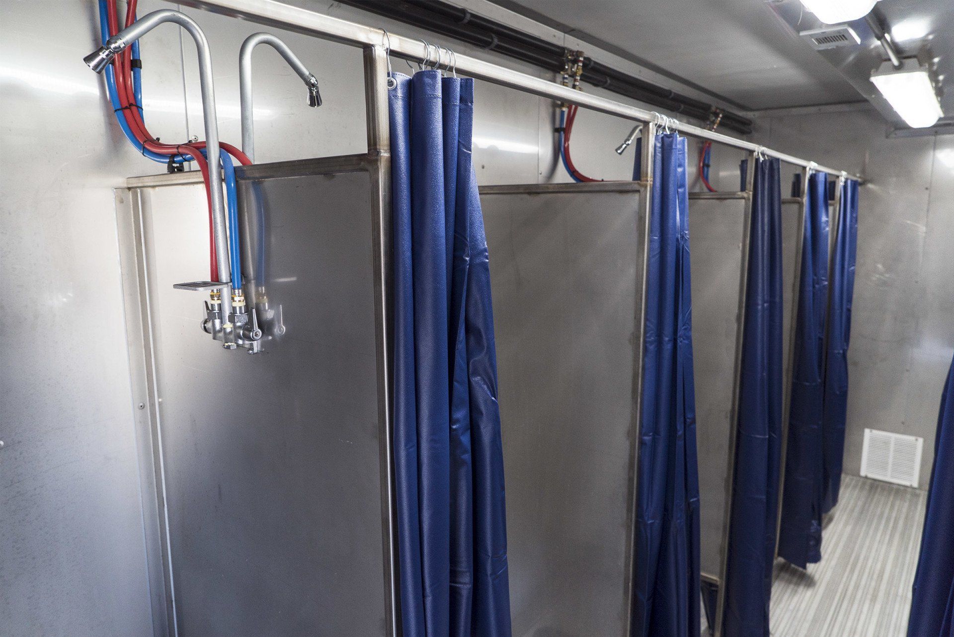 Lege industriële doucheruimte met blauwe privacygordijnen en metalen doucheslangen aan het plafond.