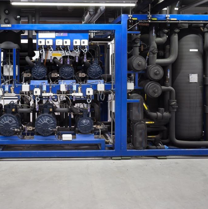 Blauwe industriële machines met leidingen, motoren en tanks in een fabriekshal.