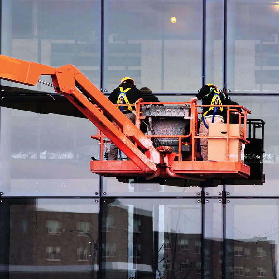 Twee werknemers in oranje hoogwerkers maken een glazen gevel van een gebouw schoon.