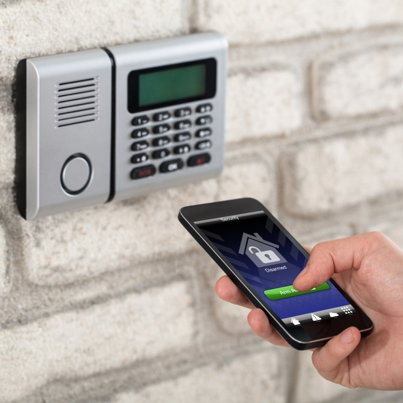 Hand die een smartphone vasthoudt in de buurt van een aan de muur gemonteerd toetsenborddeurslot met een huispictogram op het scherm.