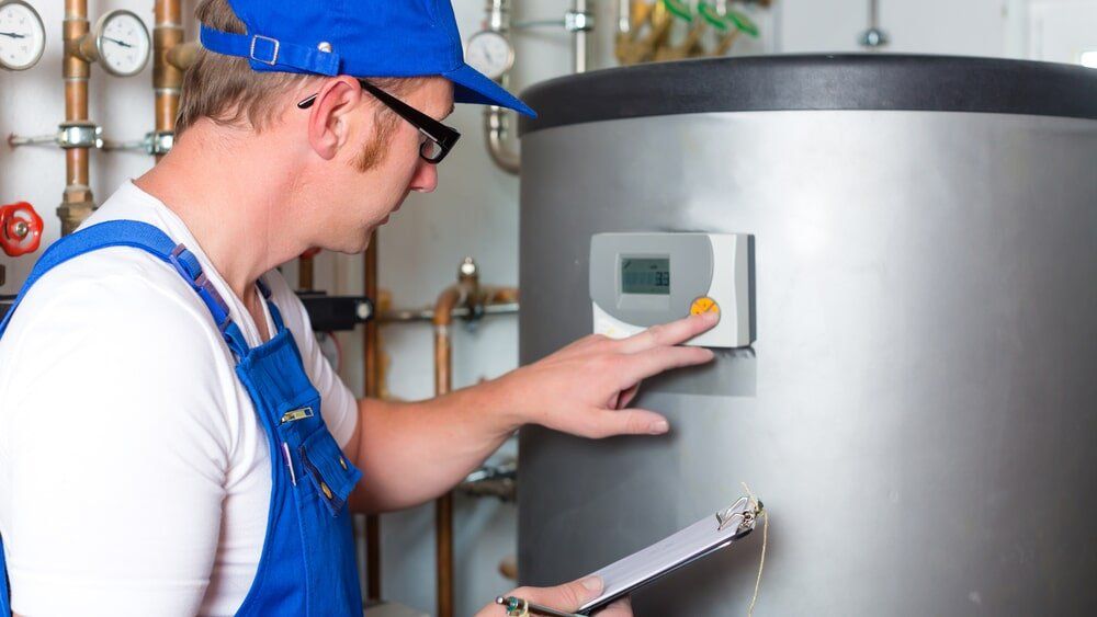 A man is working on a water heater while holding a clipboard.