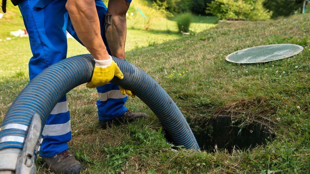 A man is pumping a hose into a septic tank.
