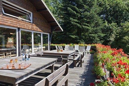 Een houten terras met tafels en banken voor een huis