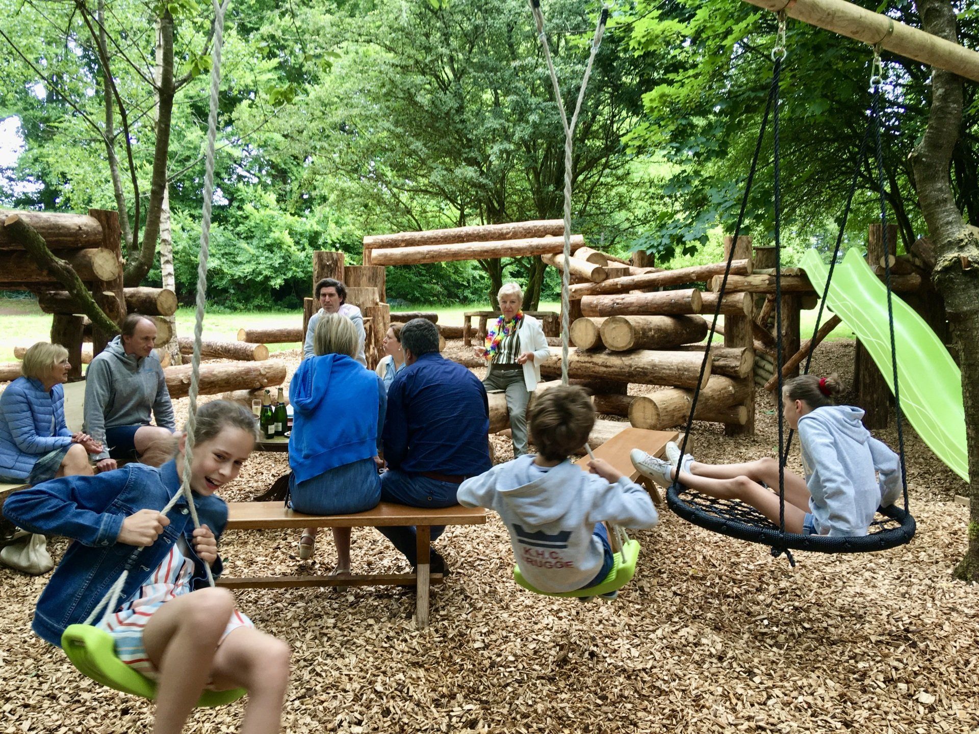 Een groep mensen zit op bankjes en schommels in een park.