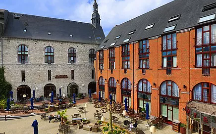 Een groot bakstenen gebouw met veel ramen en tafels en stoelen ervoor.