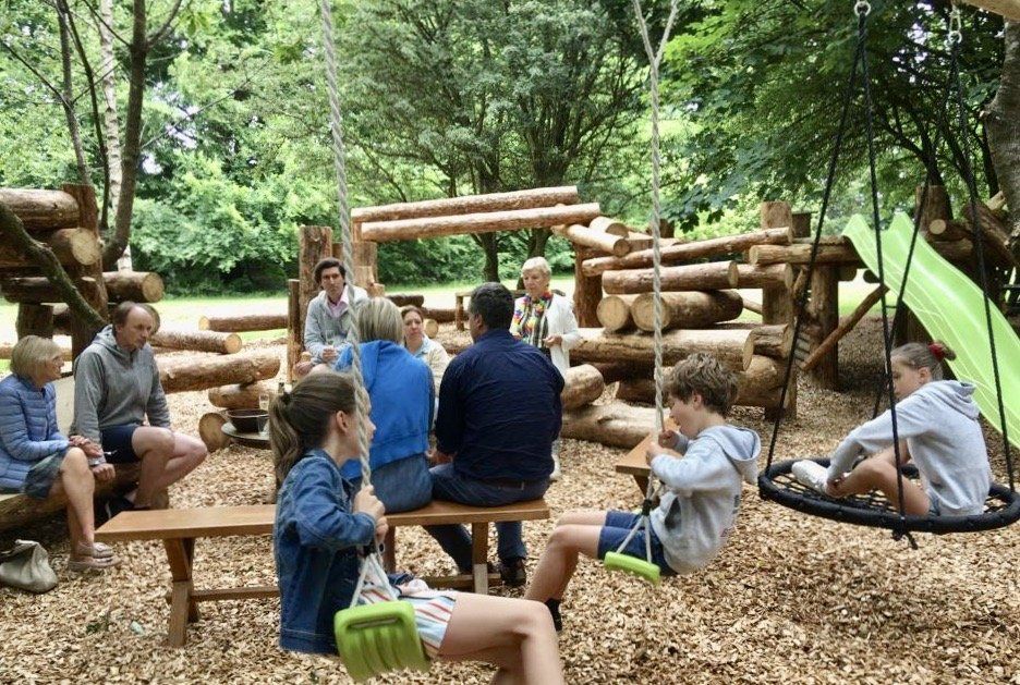 Een groep mensen zit op bankjes en schommels in een park.