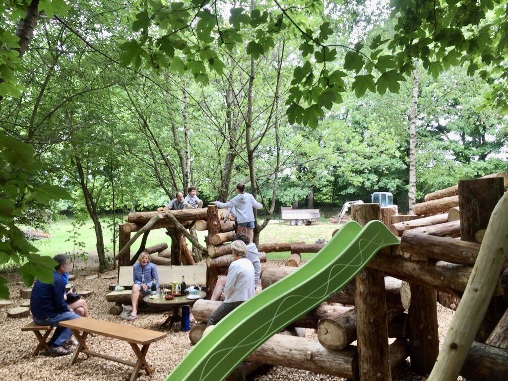 Een groep mensen zit aan een picknicktafel in het bos, vlak bij een glijbaan.