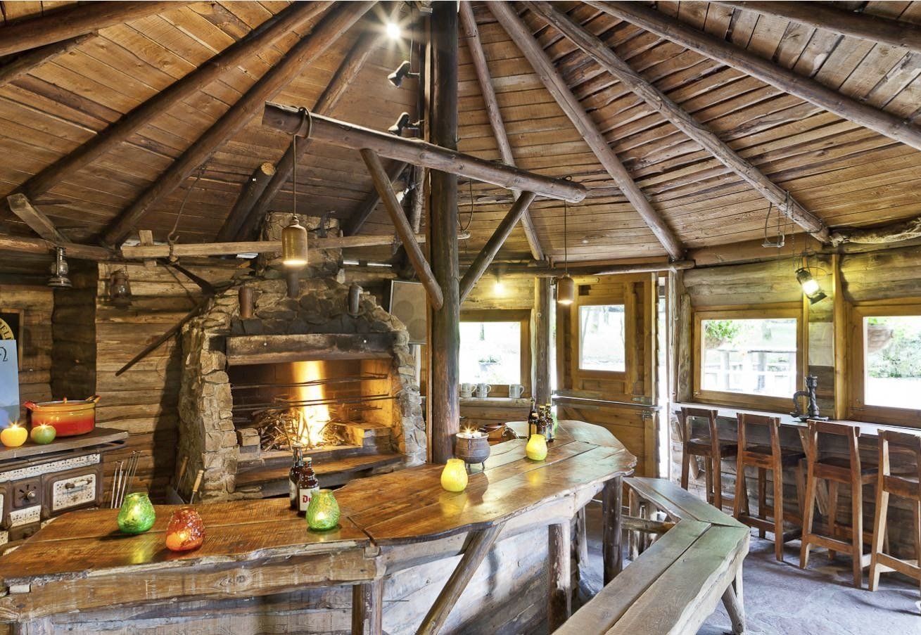 Een houten kamer met een tafel, banken en een open haard.
